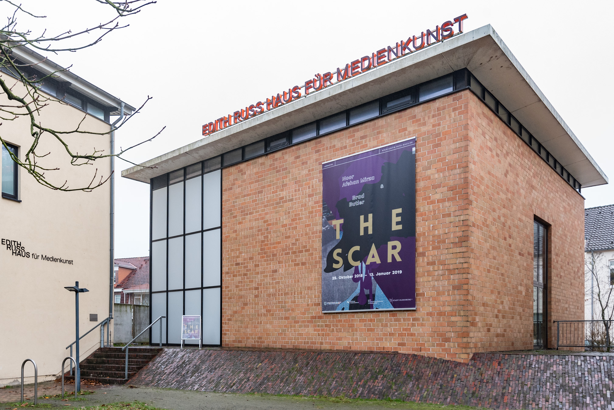 Das Foto zeigt die Fassade des Edith-Russ-Hauses mit dem Banner zu der Ausstellung Noor Afshan Mirza & Brad Butler: The Scar. Foto © Edith-Russ-Haus